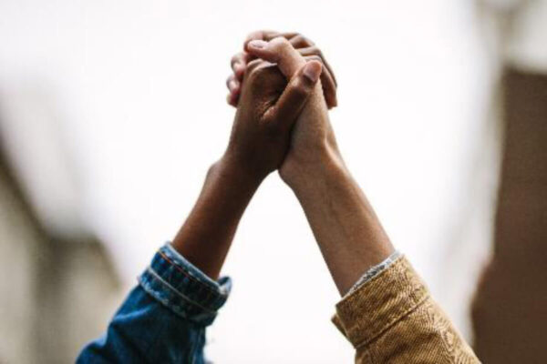 Two individuals holding hands while walking through a bustling cityscape, symbolizing unity and connection.
