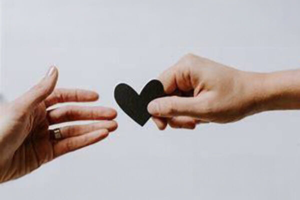 Two hands gently cradling a black heart shape, symbolizing love and compassion in a minimalist design.