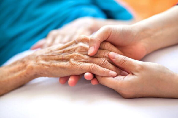 A compassionate nurse gently holds the hand of an elderly woman, conveying care and support in a warm healthcare setting.